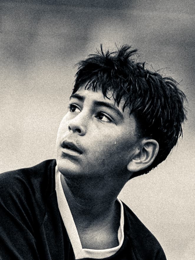 Sepia-toned close-up of a young soccer player looking up and catching his breath, hair damp with sweat.